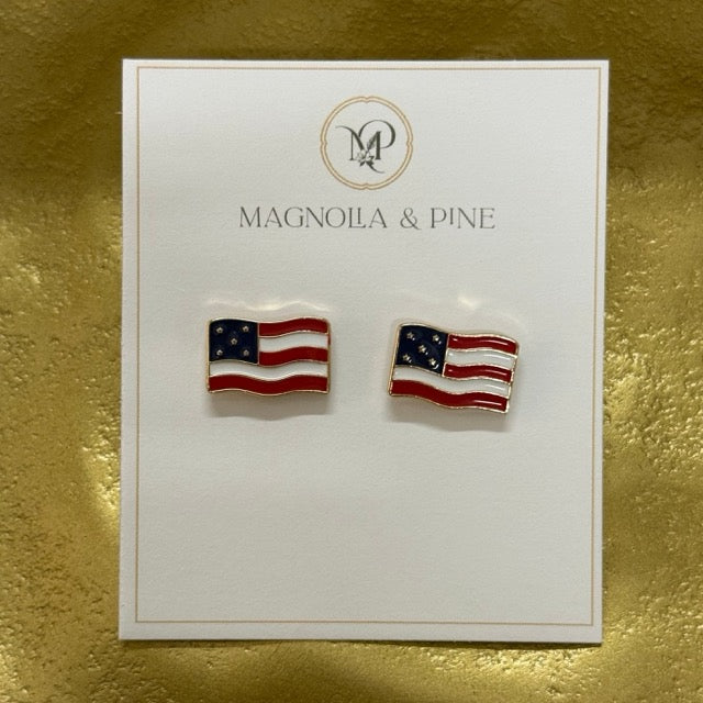 A pair of American flag stud earrings displayed on a white Magnola & Pine brand card, set against a textured gold background.