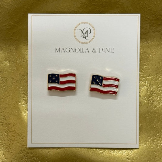 A pair of American flag stud earrings displayed on a white Magnola & Pine brand card, set against a textured gold background.