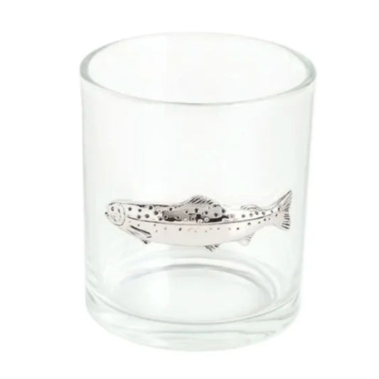 A clear glass whiskey tumbler with a silver cast-metal trout emblem on the front.
