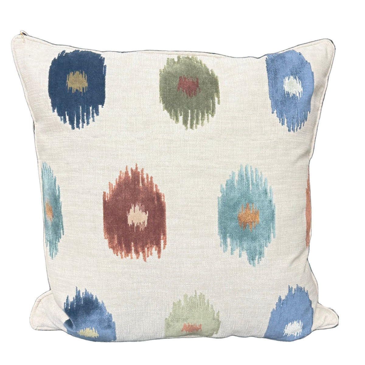 A cream pillow with an ikat-style dot print in navy, olive, rust, and teal tones.