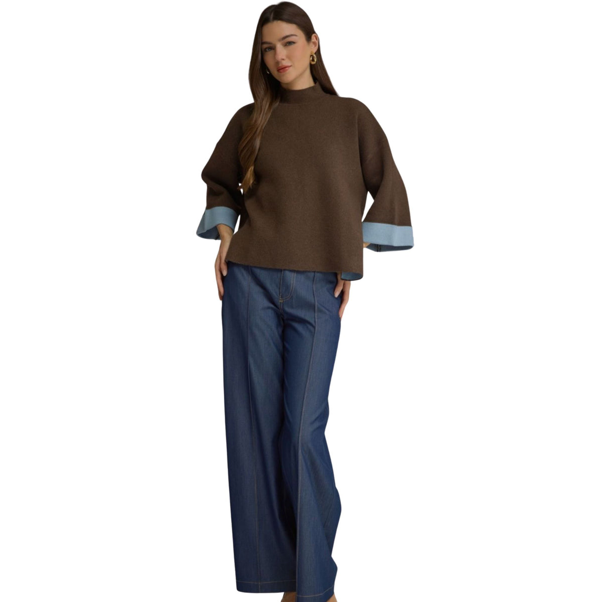 A woman wearing a brown swing sweater top with blue contrast cuffs, paired with dark wash wide-leg jeans.