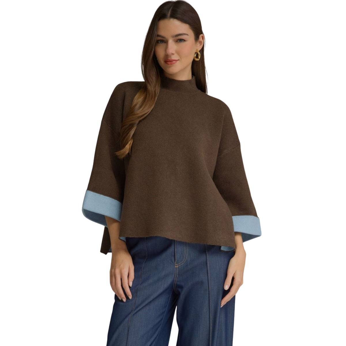 A woman wearing a chocolate brown swing sweater top with a mock neck and light blue contrast cuffs on the 3/4-length sleeves.