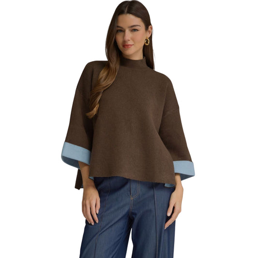 A woman wearing a chocolate brown swing sweater top with a mock neck and light blue contrast cuffs on the 3/4-length sleeves.