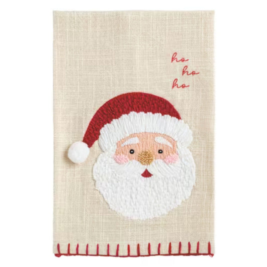 An oatmeal linen kitchen towel embroidered with a Santa face and the words 'ho ho ho' in red script, trimmed with a red whipstitch edge.