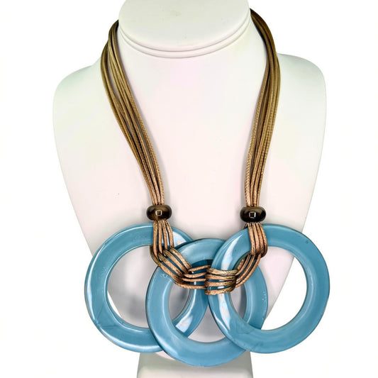 A multi-strand statement necklace displayed on a white mannequin bust. The necklace features multiple thin tan cords interlaced with three large, glossy light blue circular links, accented by small dark brown beads.