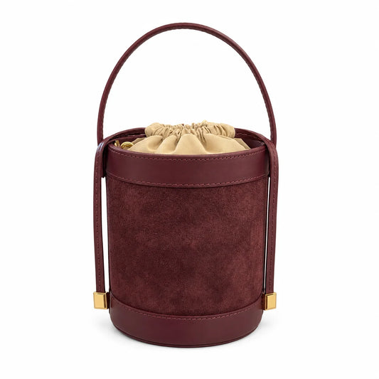 Burgundy suede bucket bag with smooth leather trim, a curved top handle with gold-tone end caps, and a cream drawstring lining.