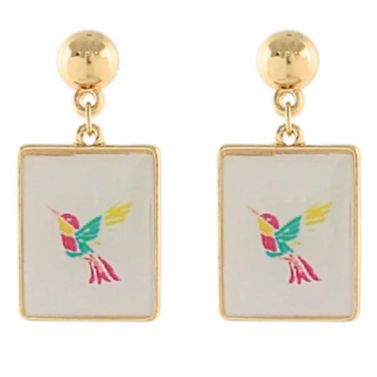 A pair of gold-tone drop earrings with gold-framed white tiles, each printed with a colorful hummingbird in pink, teal, and yellow.