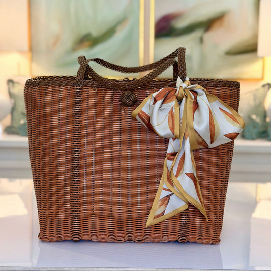 Lemon print skinny scarf wrapped around the handles of a woven wicker tote bag
