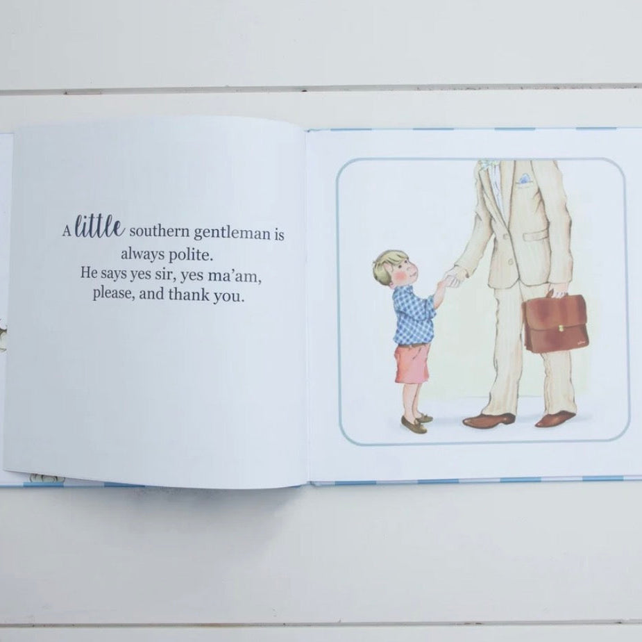An open children's picture book lying on a white wood surface. The left page has a quote about a southern gentleman, and the right page shows a small illustration of a child reaching out to a man carrying a briefcase.