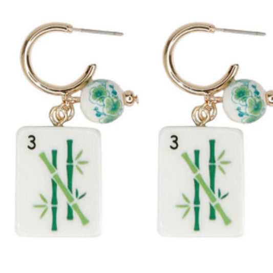 A pair of gold hoop earrings with a green-patterned bead and a white mahjong tile marked 3, showing green bamboo.