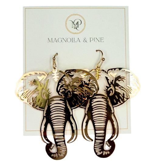 A pair of laser-cut elephant dangle earrings in a gold metallic finish, displayed on their white Magnolia & Pine brand backing card against a white background.
