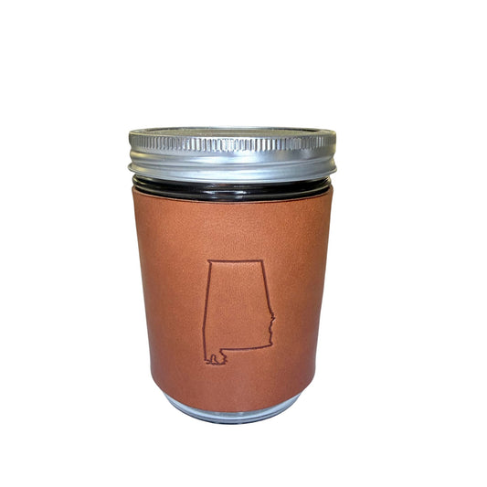 A brown leather sleeve with an embossed outline of Alabama, shown on a glass jar with a silver metal lid, isolated on a white background.