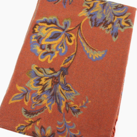 A close-up of the rust-orange scarf's woven floral pattern in blue, yellow, and brown.