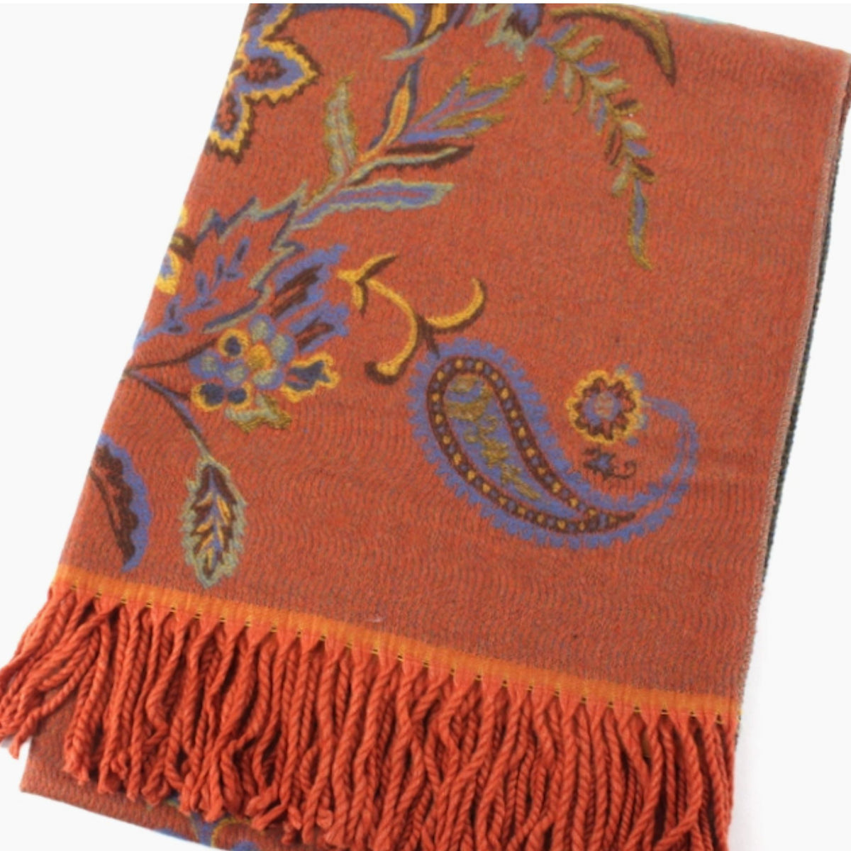 A folded rust-orange scarf with a blue, yellow, and green floral and paisley pattern, finished with fringed ends.