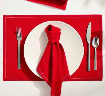 Red placemat with a white plate, folded red napkin, silver fork, knife, and spoon on a white background.