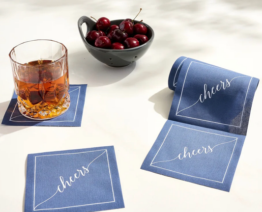 Blue cocktail napkin with a glass of whiskey and cherries on a light surface