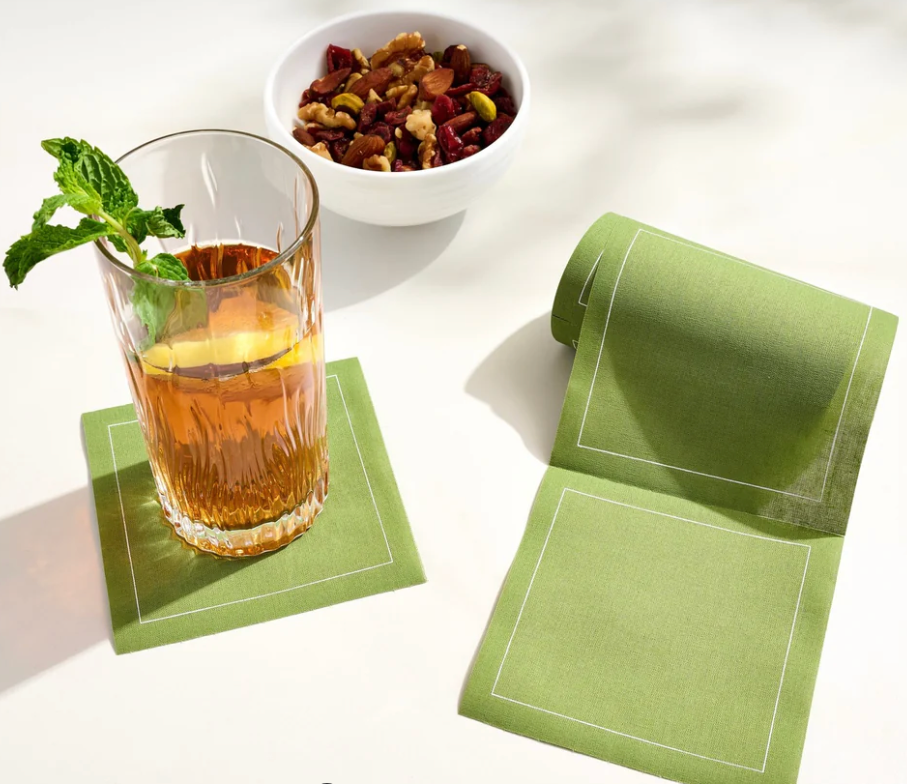 Glass of iced tea with lemon and mint, green napkin, and bowl of dried herbs on a white surface.