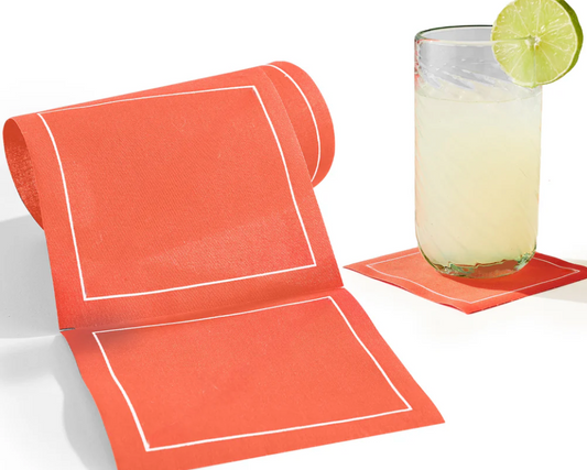 Orange-colored cotton napkins with white border on a white surface, next to a glass of lemonade with a lime wedge.