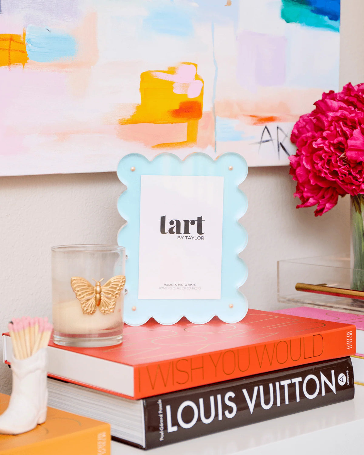 Decorative shelf with books, a candle, and an acrylic blue picture frame.