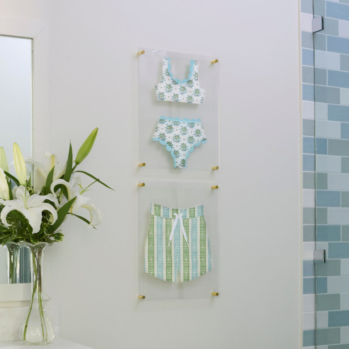 A bikini and swim trunks in coordinating green and blue prints, hand-cut and mounted as wall art on floating acrylic frames.