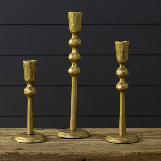 Three gold candle holders of different designs on a wooden surface with a dark background