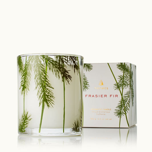 A frosted glass jar candle with green fraser fir tree illustrations, shown next to its white packaging box with matching green botanical print and gold lettering.