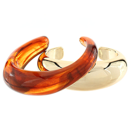A translucent amber tortoise-pattern open cuff bangle overlapping a polished gold-tone open cuff bangle.