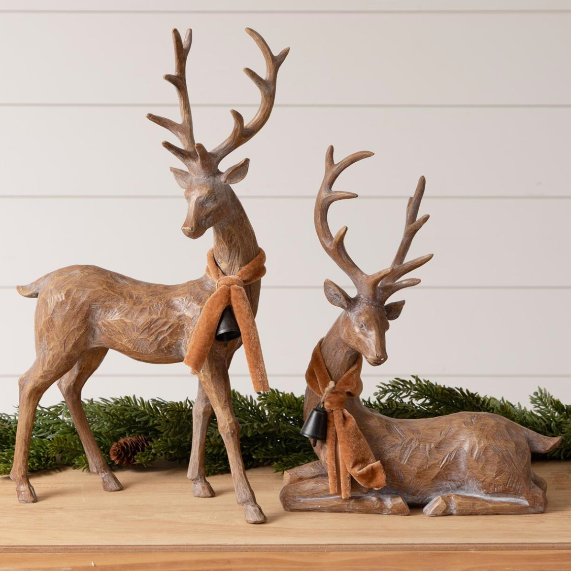 Two deer figurines with antlers on a wooden surface with a white background